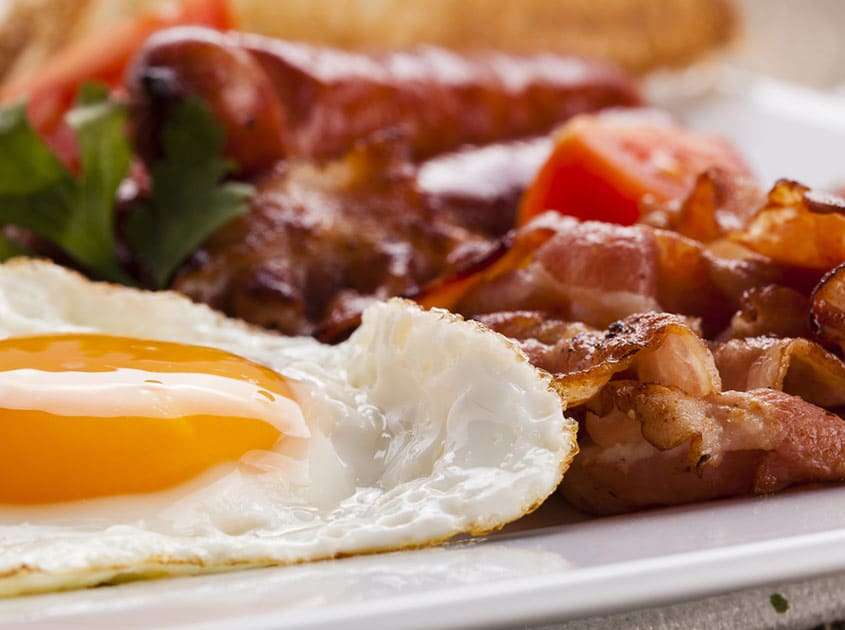Freshly cooked breakfast with a fried egg, bacon, and roasted vegetables served on a white plate.