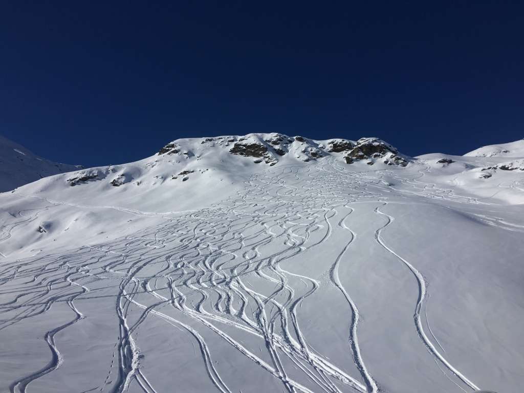 Wide-open alpine ski terrain with pristine snow and tracks leading down the mountainside.